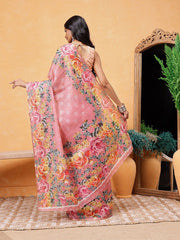 Woman wearing a pink floral saree in a room with a mirror and plants.