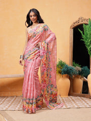 Woman wearing a pink saree with floral patterns in an indoor setting.